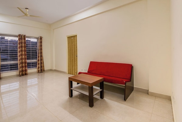 Quarto com sofá vermelho, mesa de madeira, ventilador de teto e janela com cortinas.
