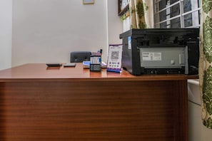 Un mostrador de recepción de madera con una impresora, un teléfono móvil, una billetera y un código QR para el pago.