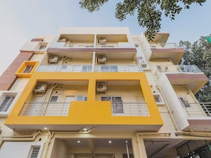 Un edificio de varios pisos con balcones, unidades de aire acondicionado y una pared de acento amarilla.
