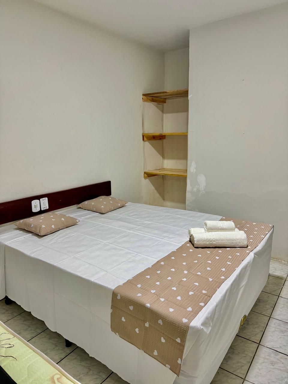 A single bed with a wooden headboard, a white bedspread, two pillows, and a brown towel on the side.
