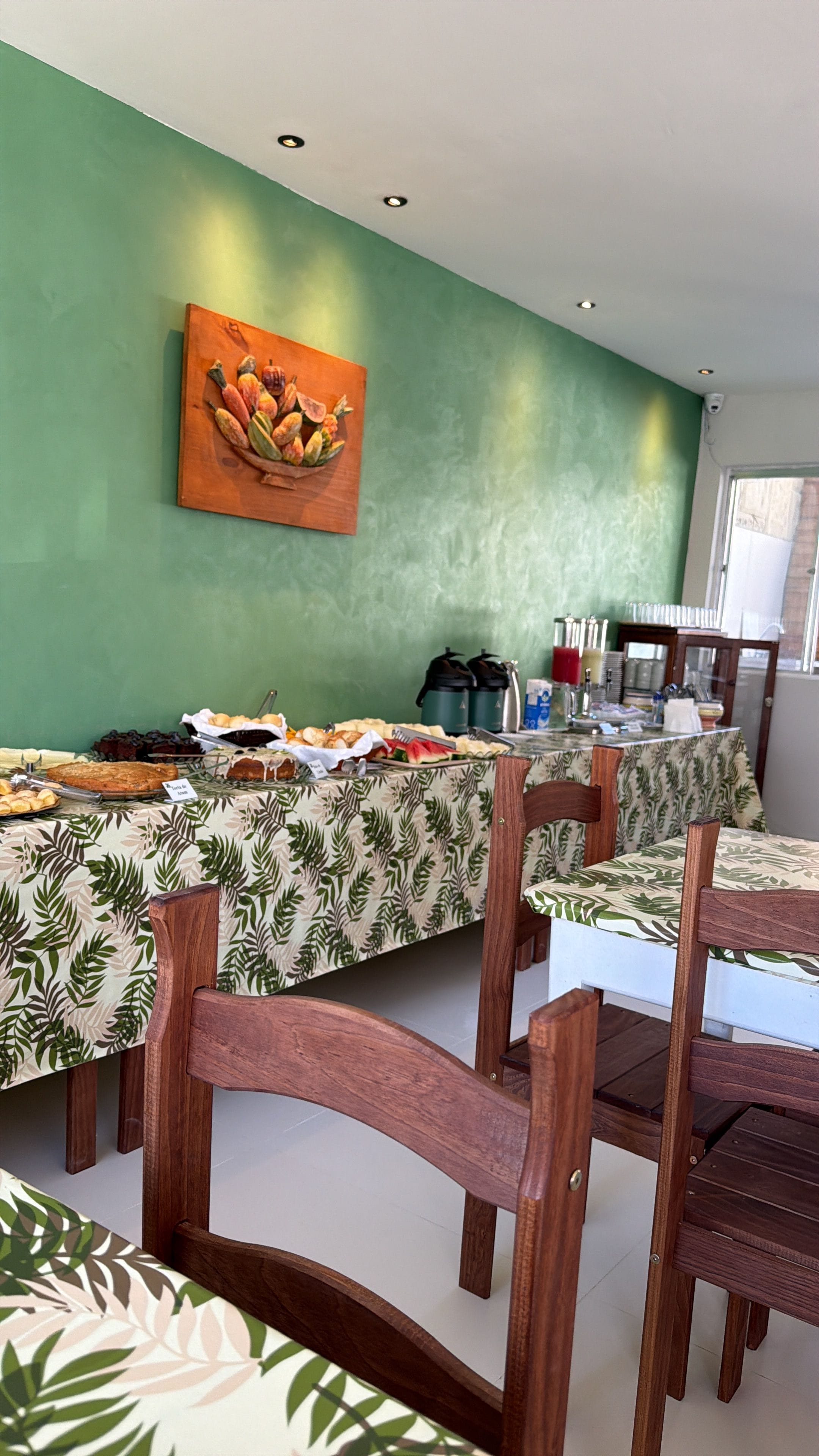 Un comedor con mesas cubiertas por manteles estampados, sillas de madera y un cuadro en la pared.