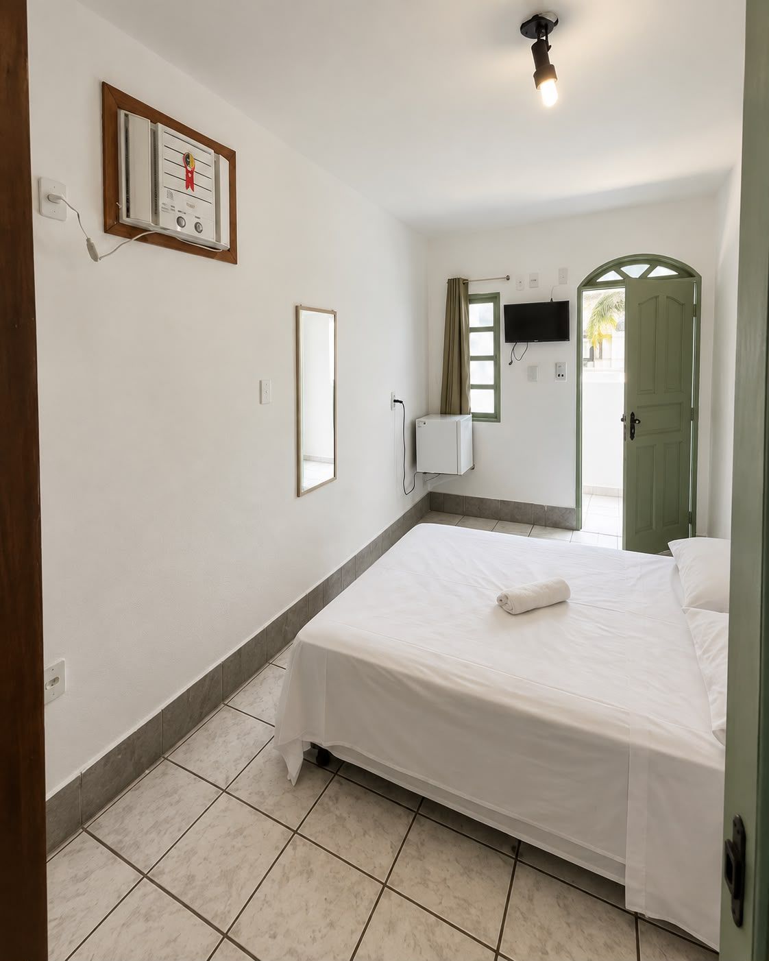 A hotel room with a bed, a television mounted on the wall, a window with curtains, and a door.