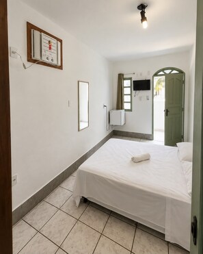A hotel room with a bed, a television mounted on the wall, a window with curtains, and a door. - JG Center Hotel Ltda (Porto Seguro)