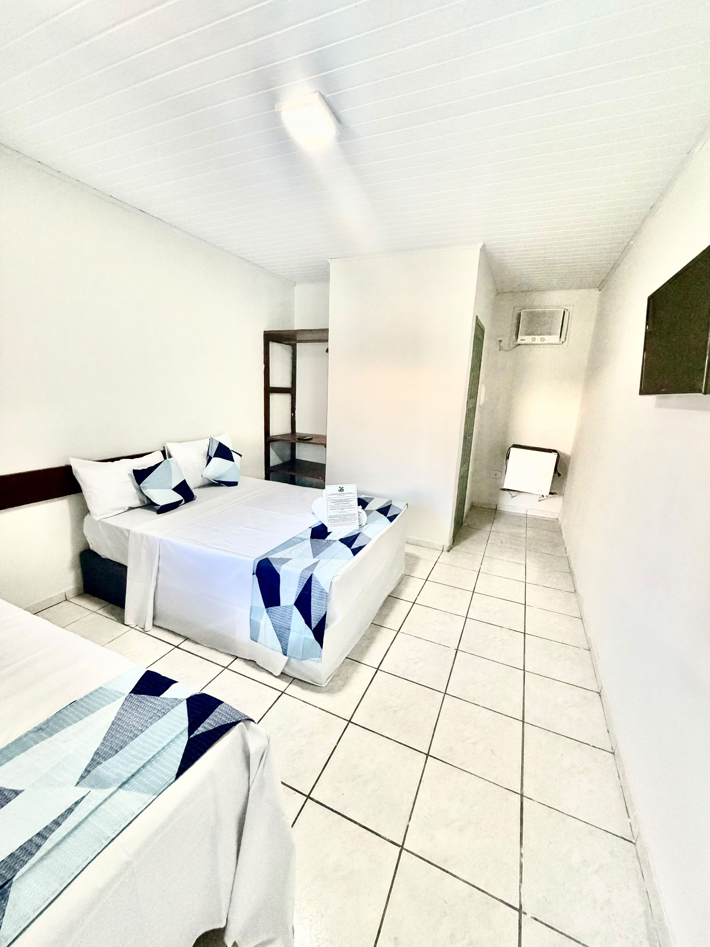 A hotel room with two beds, a small desk, a television, and a tiled floor.