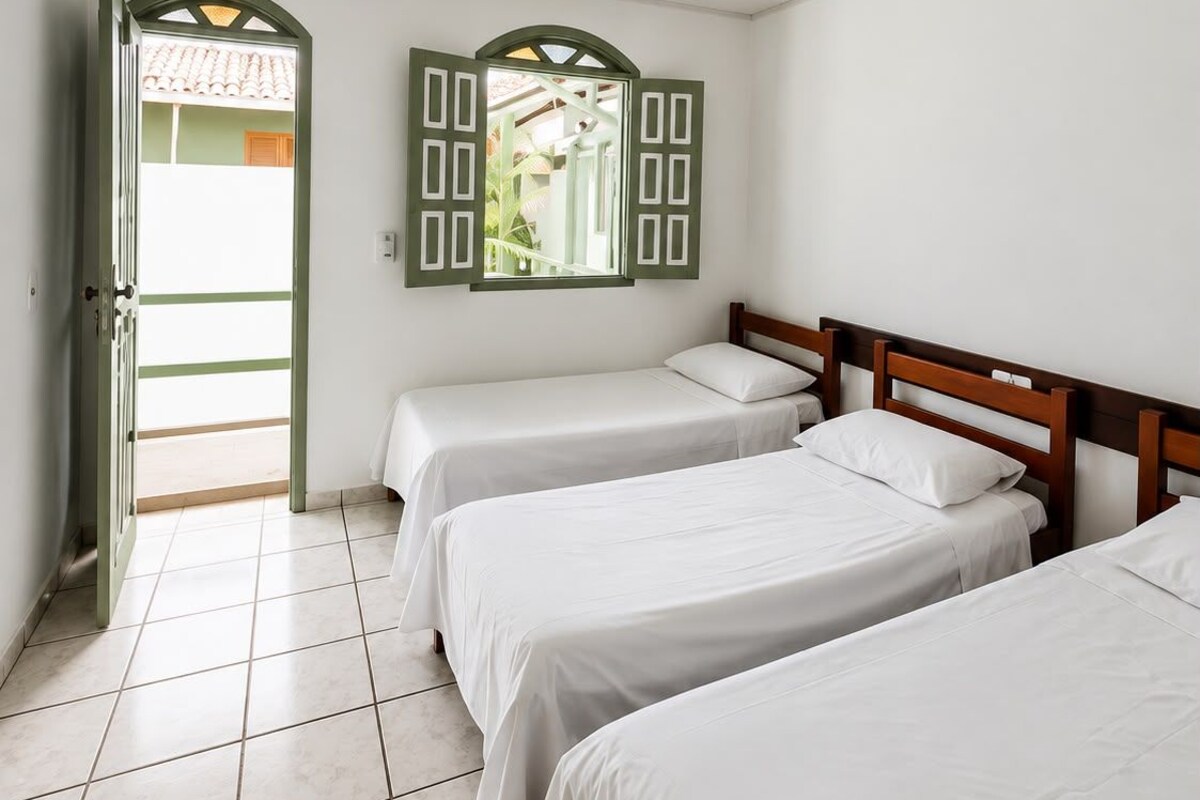 A room with three single beds, a tiled floor, a door leading outside, and a window with shutters.
