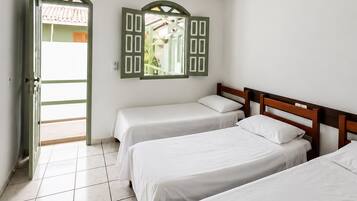 A room with three single beds, a tiled floor, a door leading outside, and a window with shutters.