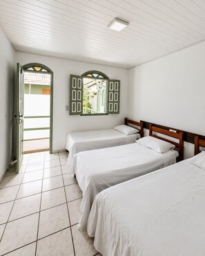 A room with three single beds, a tiled floor, a door leading outside, and a window with shutters. - JG Center Hotel Ltda (Porto Seguro)