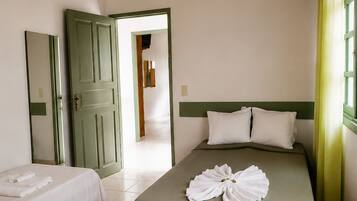 A hotel room with a bed, a smaller bed, a green door, a mirror, and a window with curtains.