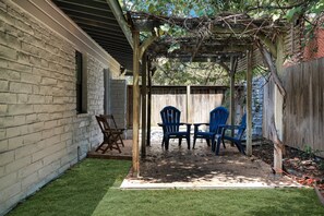 A covered patio area with a table and chairs, a brick wall, and a wooden fence. - Huge 3BR Home w/ Pool & Modern Interior (San Antonio)