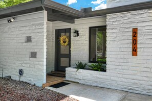 A modern house with a white brick exterior, a dark front door, and a number '204' sign on the right. - Huge 3BR Home w/ Pool & Modern Interior (San Antonio)