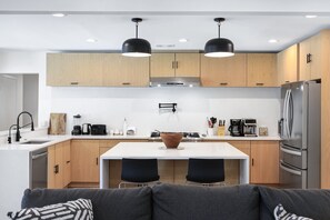 Een moderne keuken met houten kastjes, een roestvrijstalen koelkast, een koffiezetapparaat en een eethoek met een tafel en stoelen.
