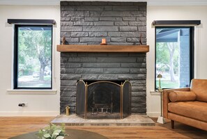 A room with a stone fireplace, a leather sofa, and large windows. - Huge 3BR Home w/ Pool & Modern Interior (San Antonio)