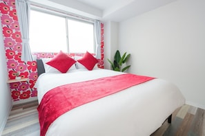 A hotel room with a large bed, a window with curtains, a plant, and a wooden floor. - [63 m²] 5 min from Dotonbori | 1 min from Kuromon Market | 3 bedrooms + sofa bed | Washer/dryer included | Sleeps up to 7 | Luggage storage available (大阪市中央区日本橋)