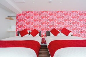 Habitación doble con papel tapiz floral, dos almohadas rojas y un perchero de madera en la pared.