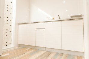 Una cocina moderna con armarios blancos, piso de madera y pileta de acero inoxidable.