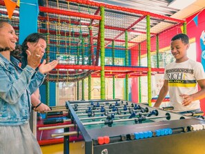 Ein Fußballtisch in einem hell erleuchteten Innenraum mit bunten Spielgeräten im Hintergrund.