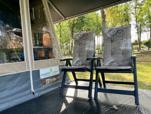 Ein Zelt mit zwei Stühlen im Inneren, ein Schild mit der Aufschrift 'Country Camp' und Blick auf Bäume.