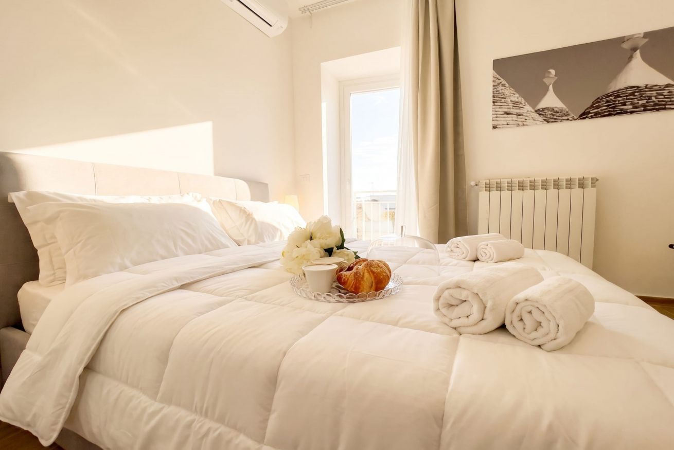 Ein ordentlich bezogenes Bett mit weißer Daunendecke, ein Tablett mit Blumen und einem Croissant sowie aufgerollte Handtücher.