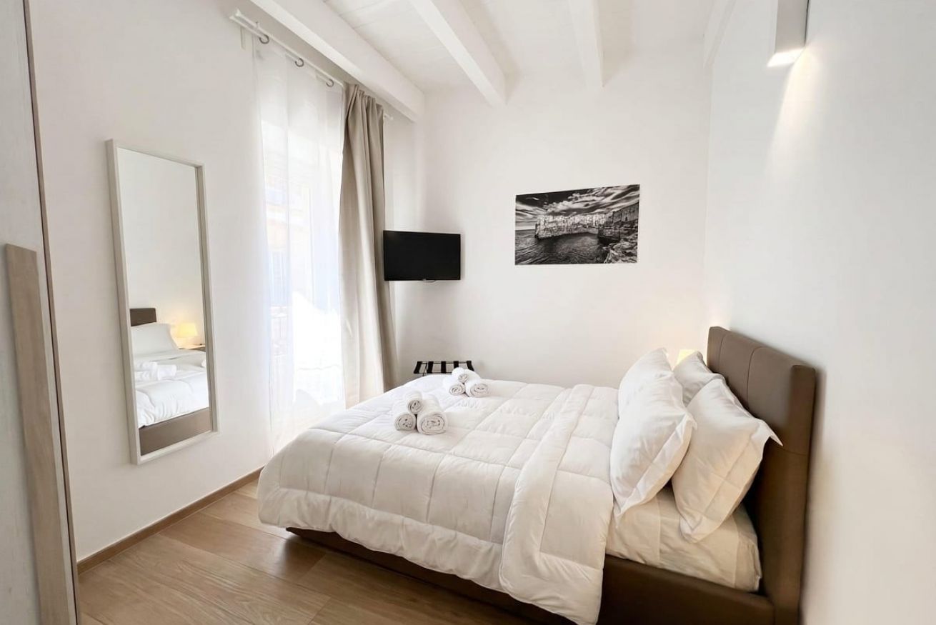 Ein Schlafzimmer mit einem Bett, einem Flachbildfernseher, einem großen Spiegel und einem gerahmten Bild an der Wand.