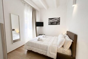Une chambre à coucher avec un lit, un téléviseur à écran plat, un grand miroir et un tableau encadré accroché au mur.