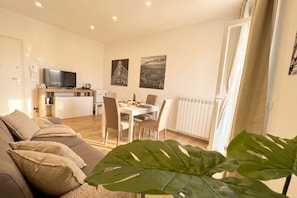Un salon moderne comprenant un canapé, une table à manger avec des chaises, un téléviseur et des œuvres d’art accrochées au mur.