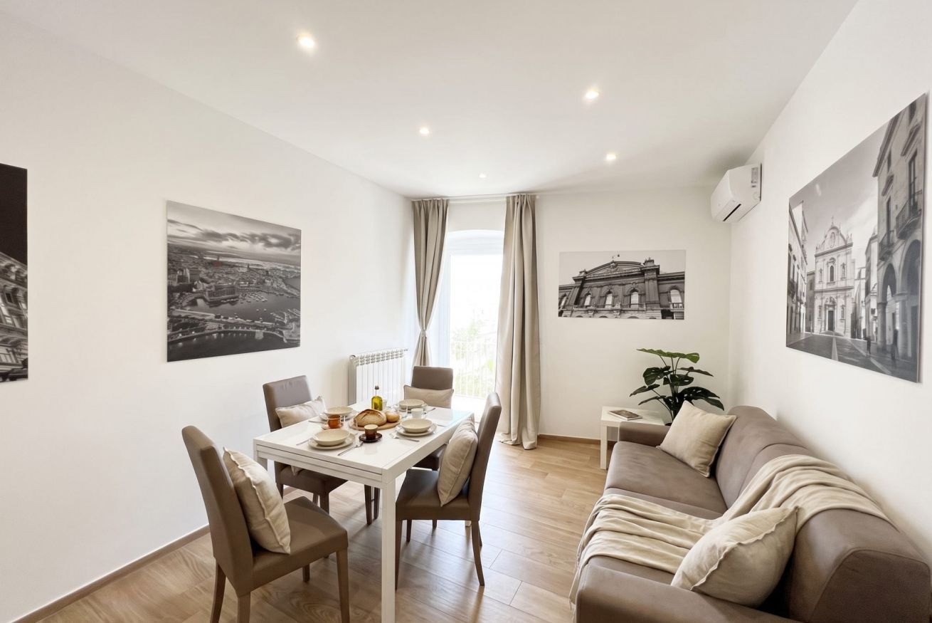Un salon moderne avec un coin repas, comprenant un canapé, une table à manger et des chaises. On y trouve également des œuvres d’art accrochées au mur et une plante en pot.