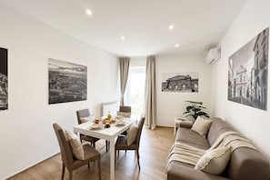 Un salon moderne avec un coin repas, comprenant un canapé, une table à manger et des chaises. On y trouve également des œuvres d’art accrochées au mur et une plante en pot.