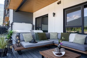 A modern outdoor seating area with a sofa, cushions, a wooden table, and potted plants. - Cabot Peak Retreat - This professionally curated, design-forward condo is your perfect basecamp, located just minutes from both downtown and the world-class slopes of Revelstoke Mountain Resort. (Revelstoke)