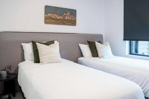 A hotel room with two beds, a nightstand, a small potted plant, and a painting of mountains on the wall. - Cabot Peak Retreat - This professionally curated, design-forward condo is your perfect basecamp, located just minutes from both downtown and the world-class slopes of Revelstoke Mountain Resort. (Revelstoke)