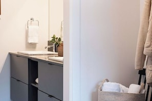 A modern bathroom with a sink, mirror, towel rack, and a plant. - Cabot Peak Retreat - This professionally curated, design-forward condo is your perfect basecamp, located just minutes from both downtown and the world-class slopes of Revelstoke Mountain Resort. (Revelstoke)