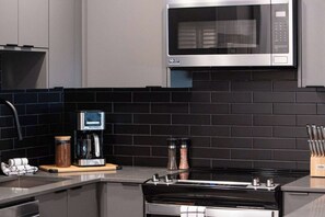 A modern kitchen with a microwave, coffee maker, and stove. - Cabot Peak Retreat - This professionally curated, design-forward condo is your perfect basecamp, located just minutes from both downtown and the world-class slopes of Revelstoke Mountain Resort. (Revelstoke)