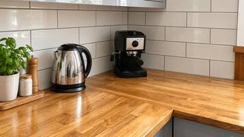 A kitchen with a wooden countertop, a coffee maker, a kettle, and a potted plant.