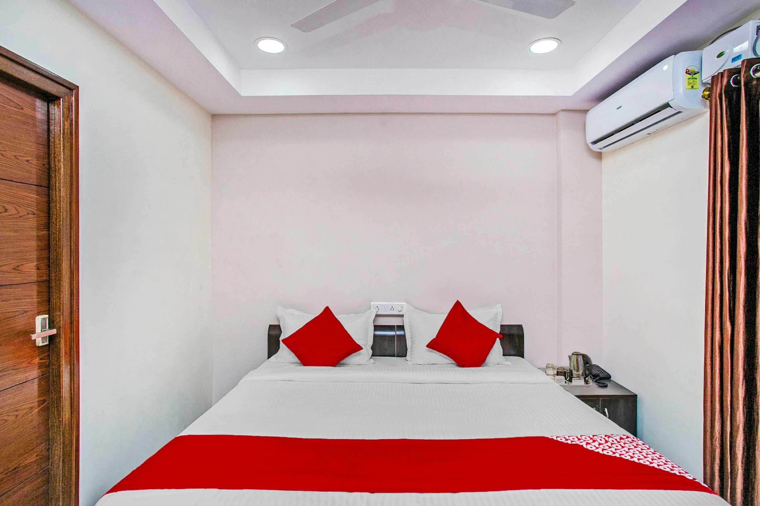 A hotel room with a bed, a nightstand, an air conditioning unit, and a wooden door.