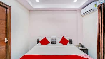 A hotel room with a bed, a nightstand, an air conditioning unit, and a wooden door.