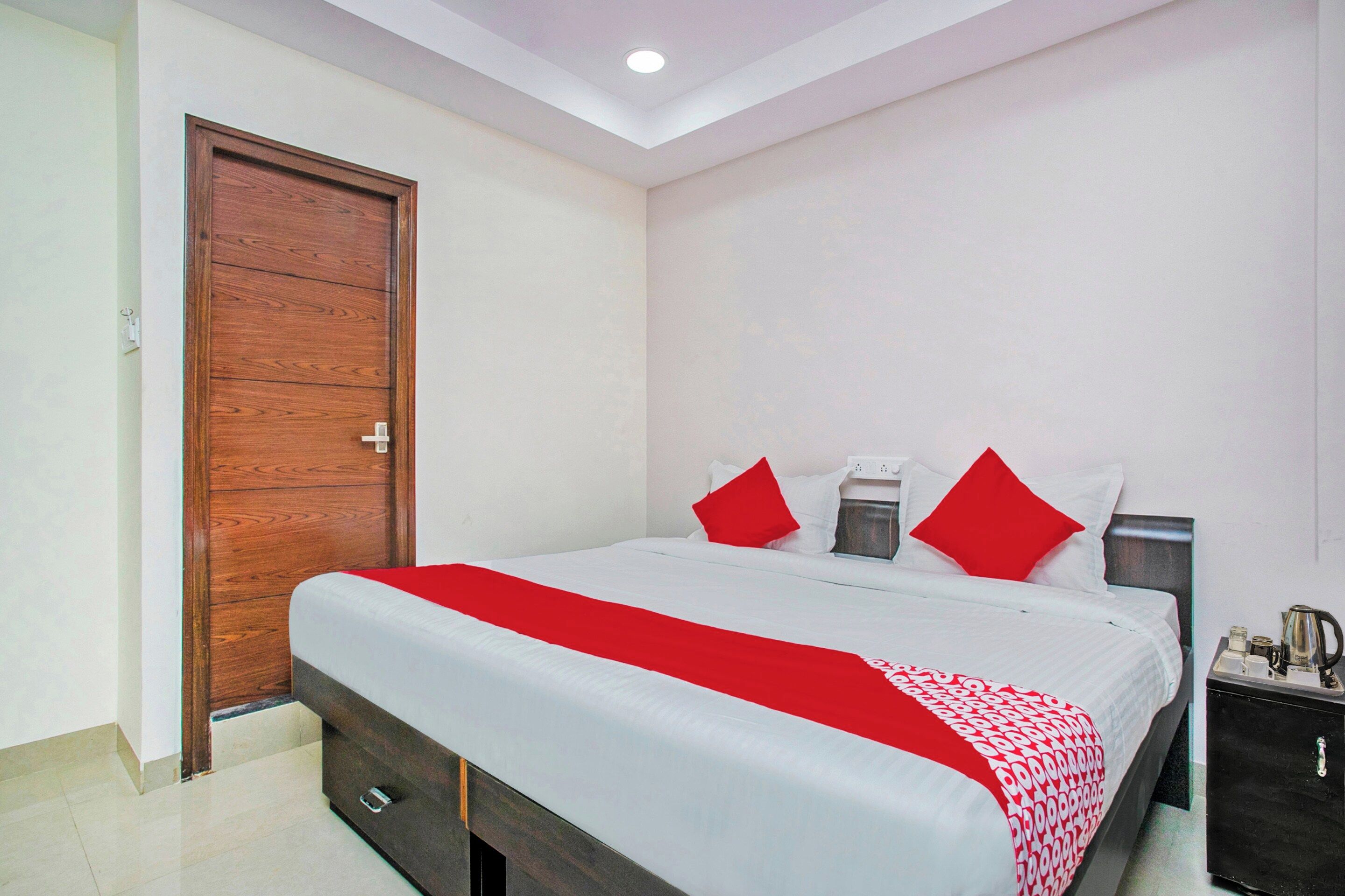 A hotel room with a large bed, a wooden door, a bedside table with a lamp, and a small cabinet.