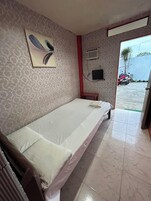 Una cama individual en una habitación con papel tapiz estampado, un televisor en la pared y una puerta que da al exterior.