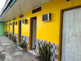 Fila de habitaciones de hotel con equipos de aire acondicionado, entrada con azulejos y plantas en macetas.