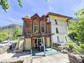 Ein zweigeschossiges Holzhaus mit Steinaußenseite, einem Balkon und Blick auf eine gebirgige Landschaft.