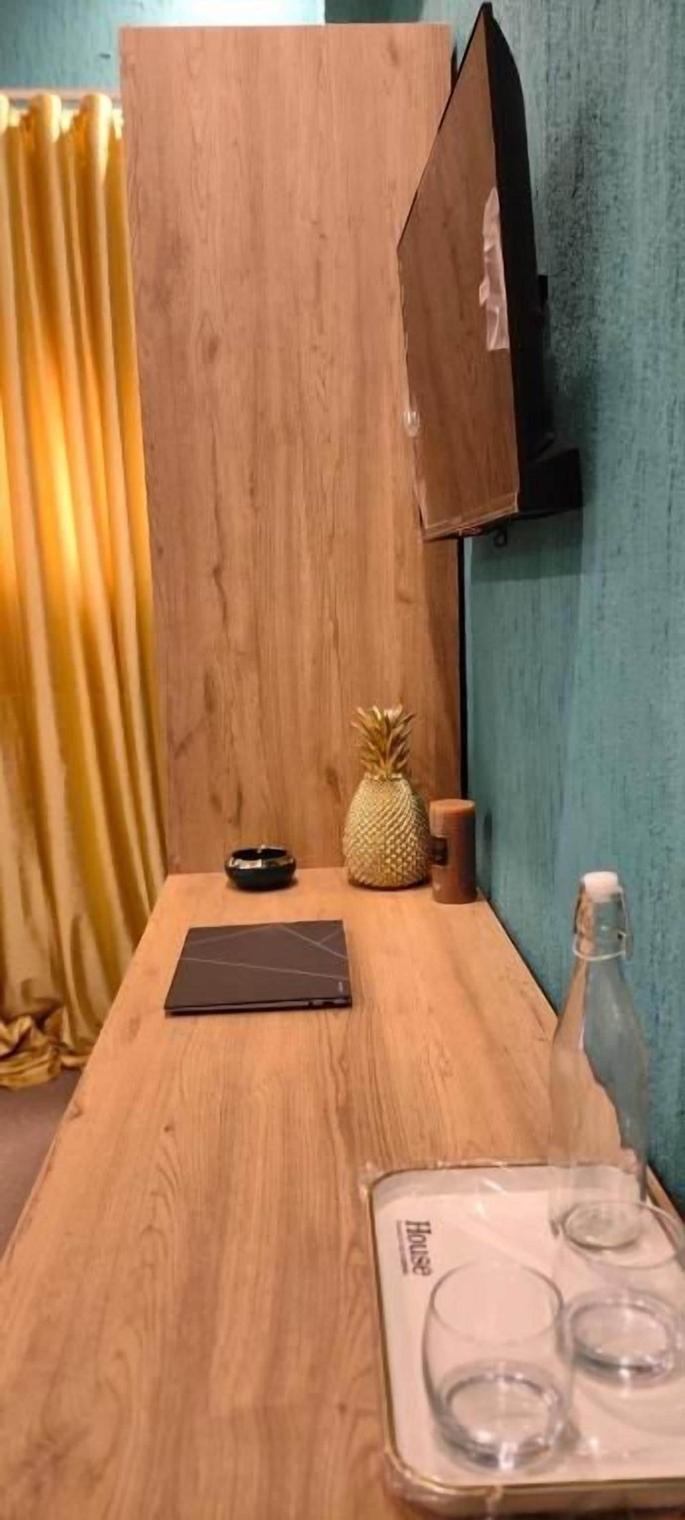 A wooden table with a laptop, a pineapple, a bottle, and a tray with glasses.