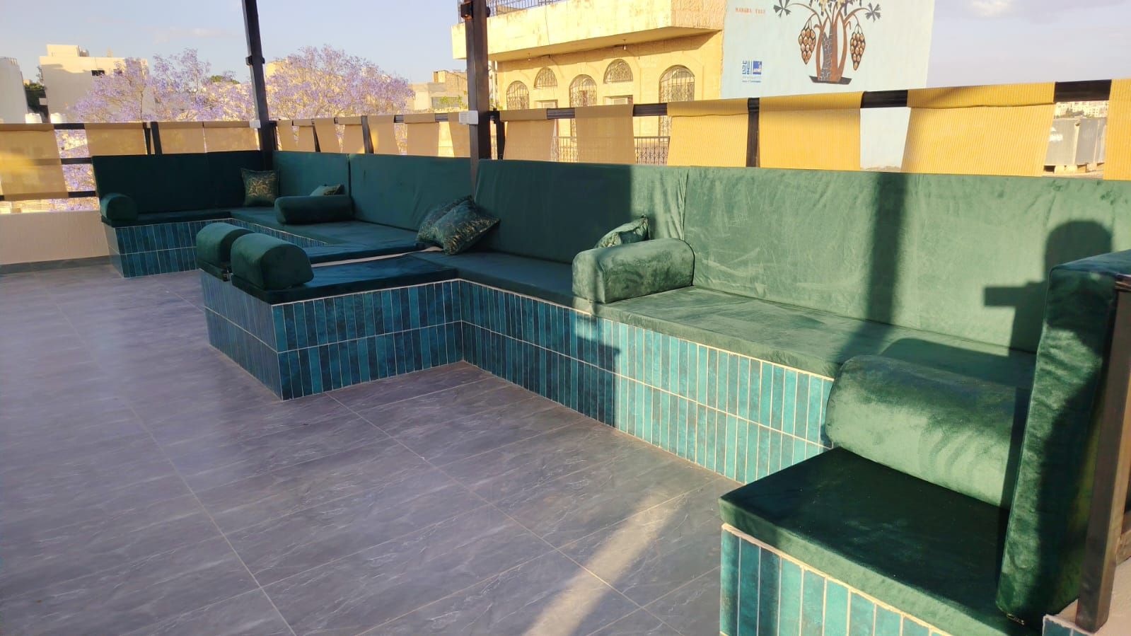 Una terraza en la azotea con un área de estar acolchada de color verde y suelo de baldosas.