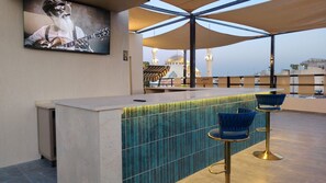 A bar area with a tiled backsplash, a television mounted on the wall, and a view of a mosque in the background. - BLUE STONE H (Madaba)