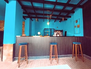 Zona de bar con pared azul, taburetes de madera y una barra.