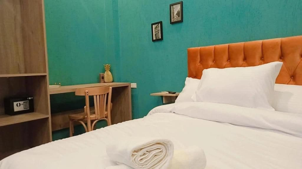 A hotel room with a bed, a desk, a chair, and a shelf with a radio.