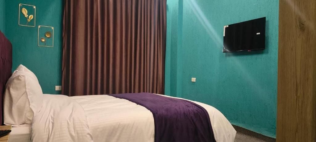 A hotel room with a bed, curtains, a television, and wall decorations.
