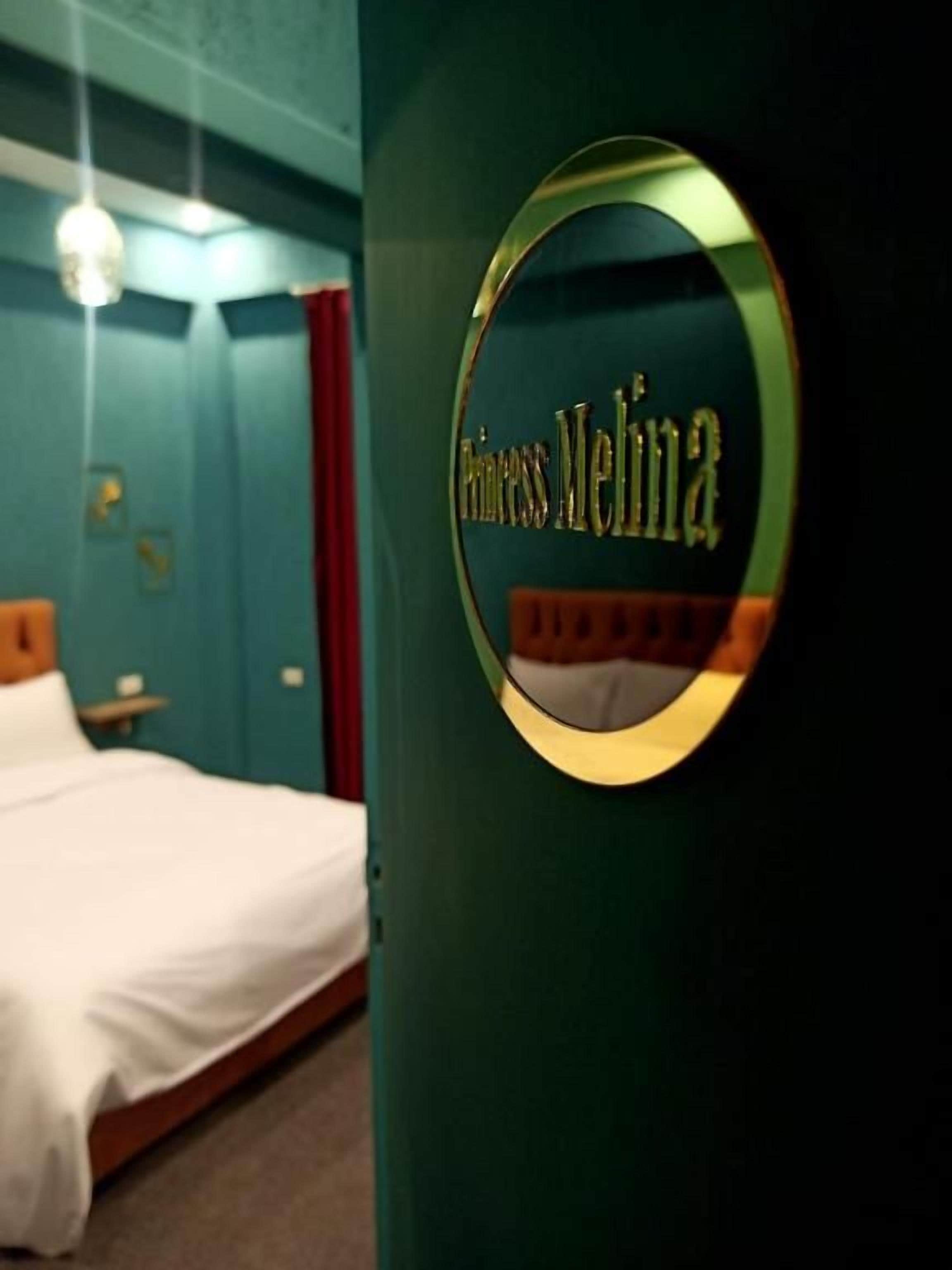 Een rond bord met de tekst 'Princess Meliha' in een kamer met een bed en een nachtkastje.