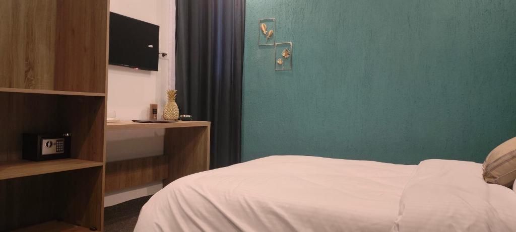 A bedroom with a bed, a desk with a computer, a television on the wall, and a shelf with a radio.