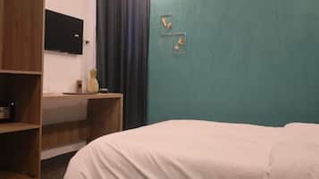A bedroom with a bed, a desk with a computer, a television on the wall, and a shelf with a radio.