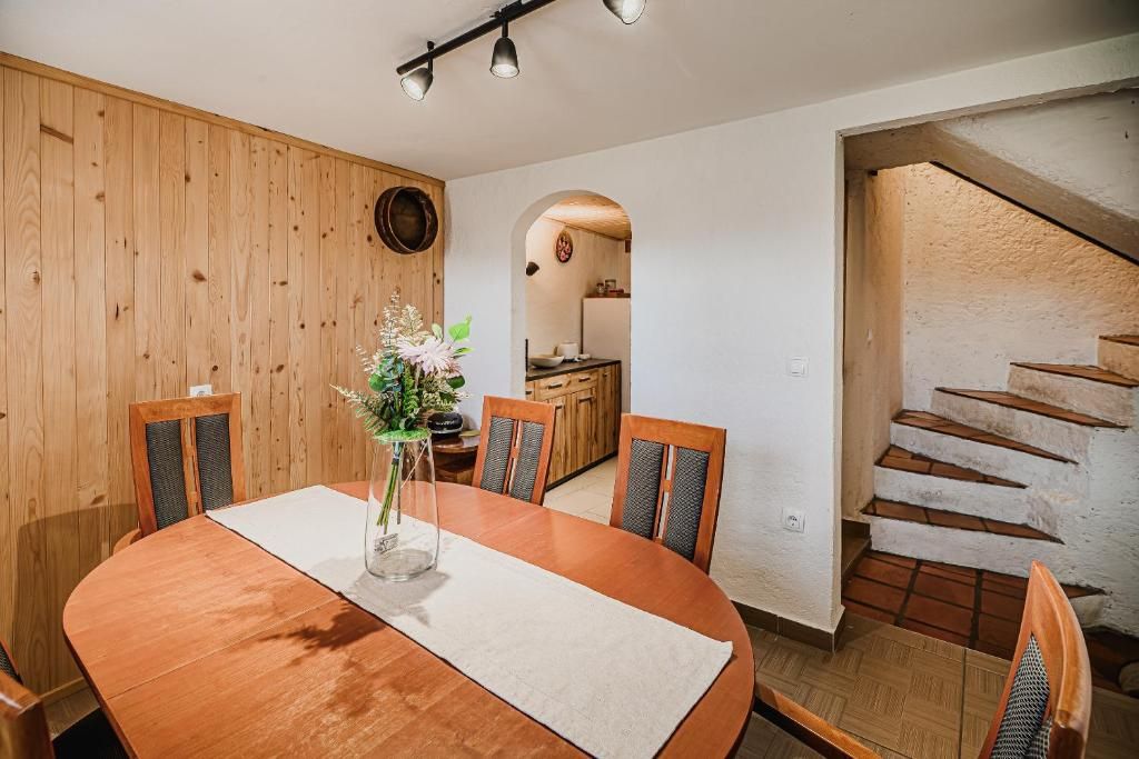 Un coin repas avec une table et des chaises en bois, un vase rempli de fleurs et une cuisine visible à travers une arche.