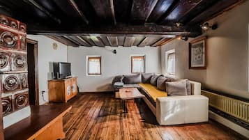 Una sala de estar acogedora con piso de madera, un sofá, un reposapiés blanco, una mesa de centro de madera y un televisor sobre un mueble.