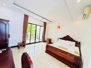 A bedroom with a large bed, a wooden nightstand, a desk, and a chair. There is a sliding glass door leading to a balcony. - ORA Boutique (Siem Reap)